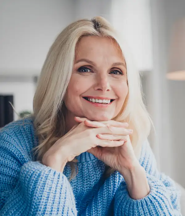 mature woman in blue crochet sweater smiling with hands under her chin